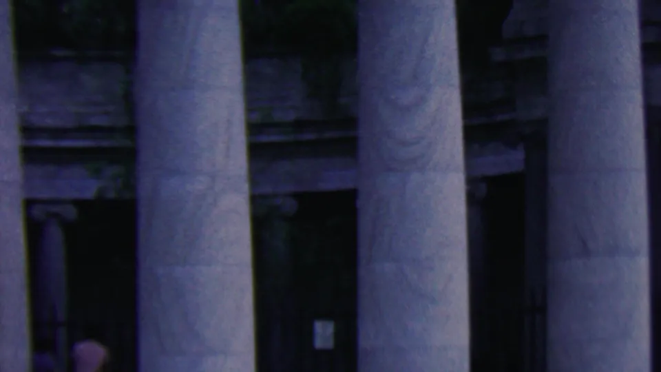 1961 Covington, Kentucky home-movie frame showing tall fluted columns, shadowed entry bays, and a small figure partly visible near the left doorway.