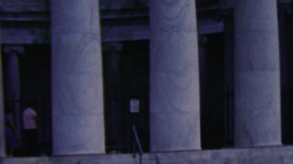 1961 Covington, Kentucky home-movie frame of a grand classical facade with large fluted columns and a person in a light shirt standing in a shadowed doorway.