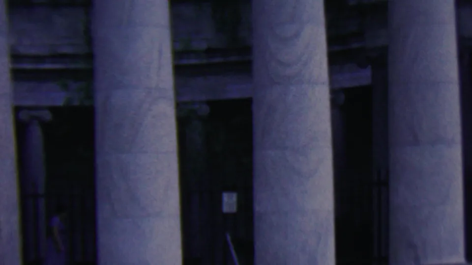 1961 Covington, Kentucky home-movie frame showing the lower portion of tall columns, dark entrances, and a small person partly visible near the edge of the frame.