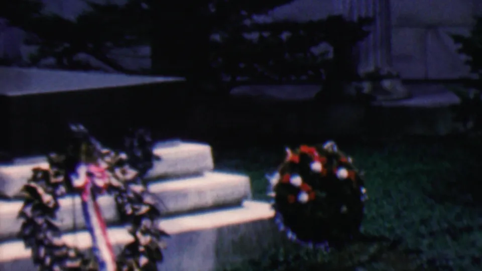 Covington, Kentucky 1961 8mm frame with multiple wreaths and patriotic ribbons positioned on pale stone steps near a monument.