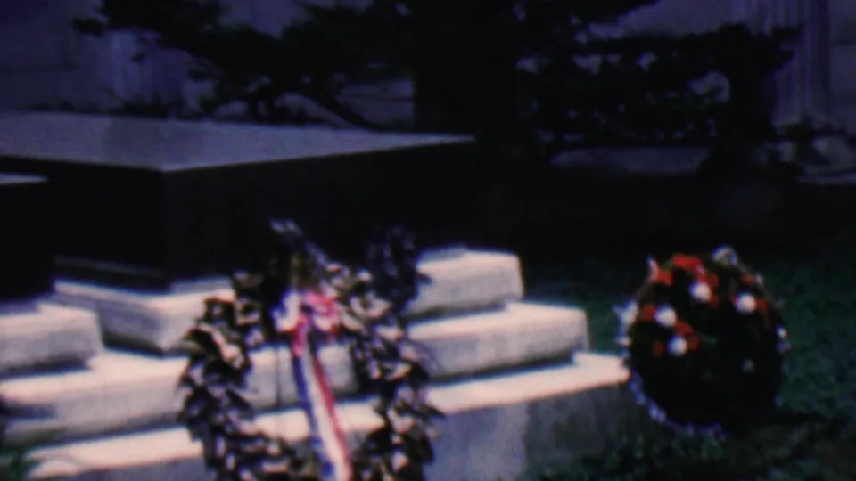Covington, Kentucky, 1961 home-movie frame showing floral wreaths with a ribbon beside stone steps at an outdoor memorial site.