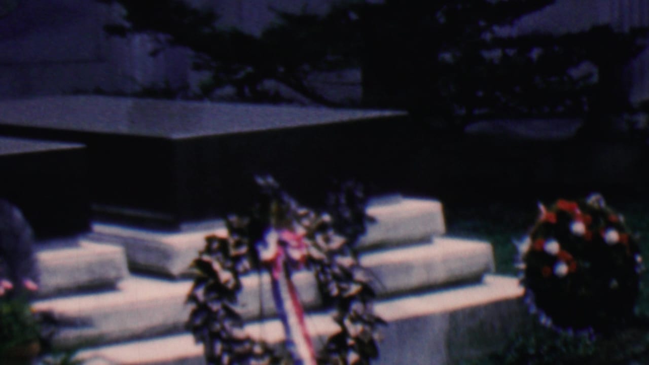 Stone steps, dark monument base, and two wreaths in a shaded outdoor setting.
