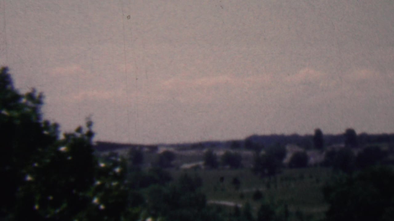 1961 Covington, Kentucky home-movie frame showing distant rolling hills, scattered trees, and a muted overcast sky in soft 8mm color.