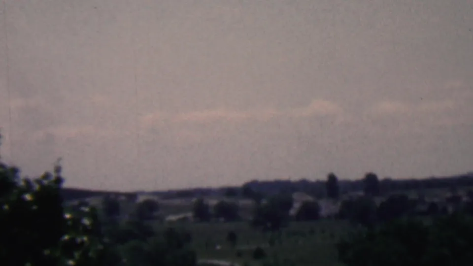 A soft 8mm view from the Covington, Kentucky clip shows dark foreground trees, distant hills, and a pale clouded sky.