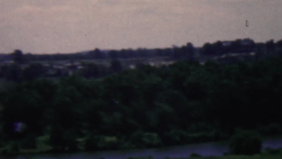 The final sampled frame shows dense foreground trees, a calm body of water, and distant wooded hills in the 1961 Covington, Kentucky landscape footage.