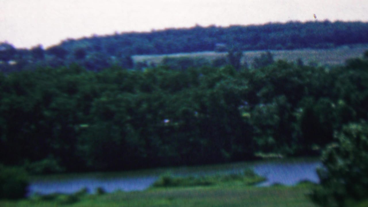 Tree-lined water with distant wooded ridge and open fields.