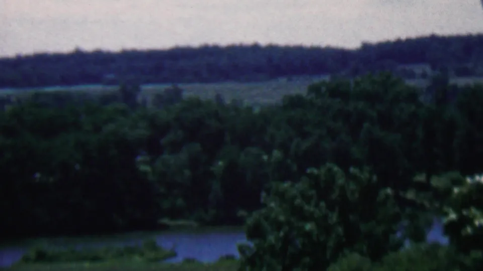 Final frame of the short landscape view, with dense green trees, a calm lake, and dark wooded hills in the distance, consistent with the supplied 1961 Covington, Kentucky metadata.