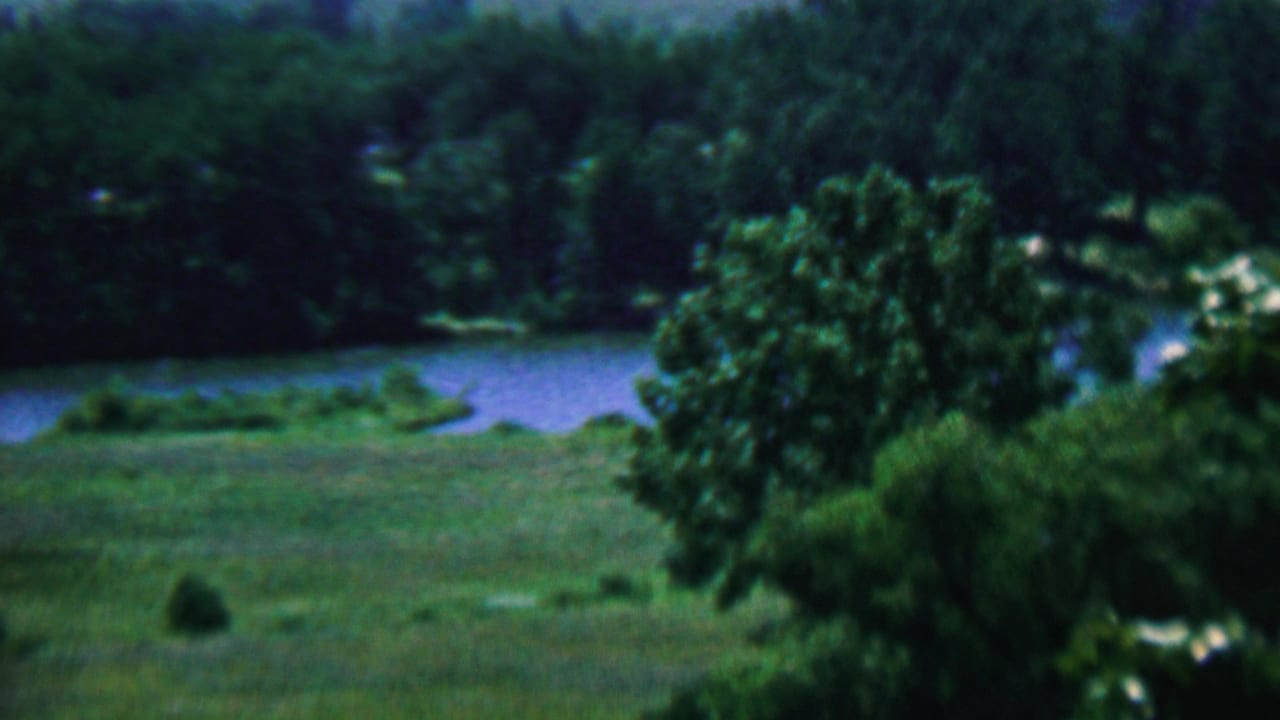 A soft 1961 8mm view of green parkland in Covington, Kentucky, with trees and a winding body of water beyond the field.