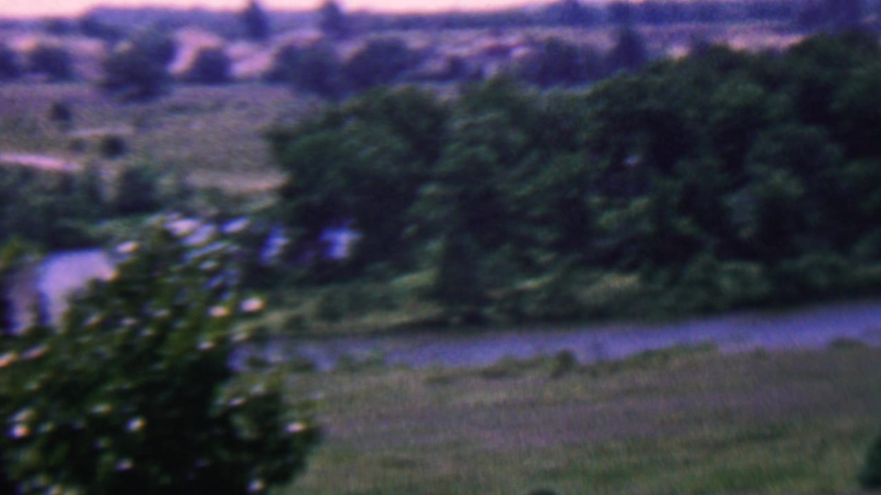 1961 Covington, Kentucky 8mm frame showing a soft-focus river or stream bordered by trees, grass, and distant rolling terrain.