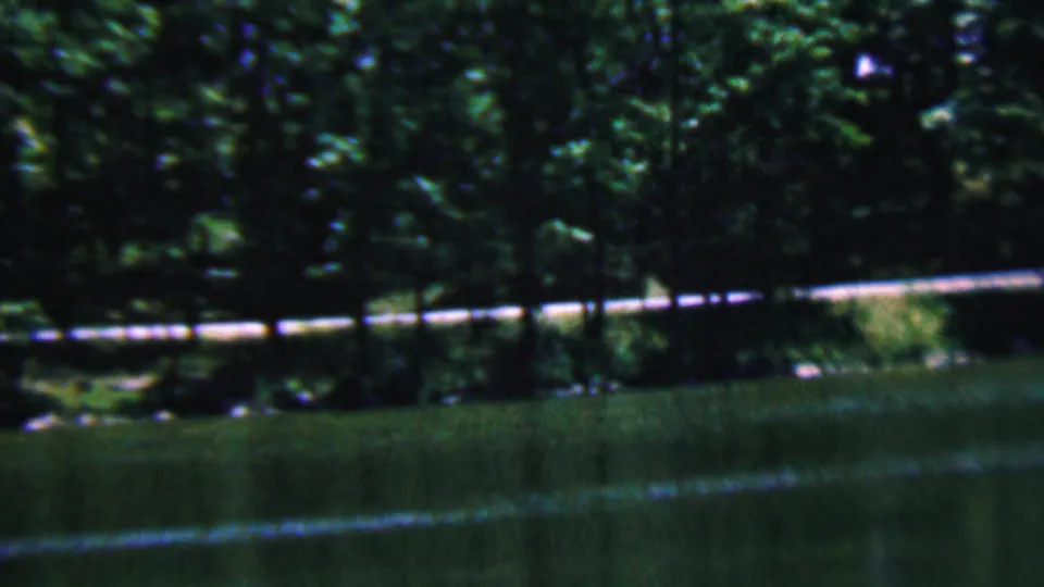 1961 Covington, Kentucky 8mm frame showing a wooded riverbank, green water, and a pale fence or rail running horizontally near the trees.