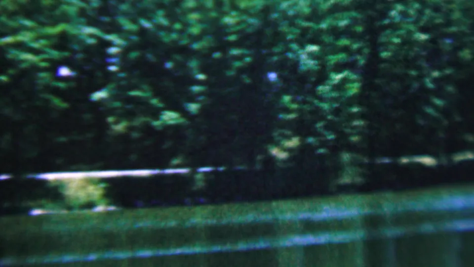 1961 Covington, Kentucky 8mm frame showing a blurred wooded bank, green river water, and a light-colored fence or rail partly obscured by foliage.