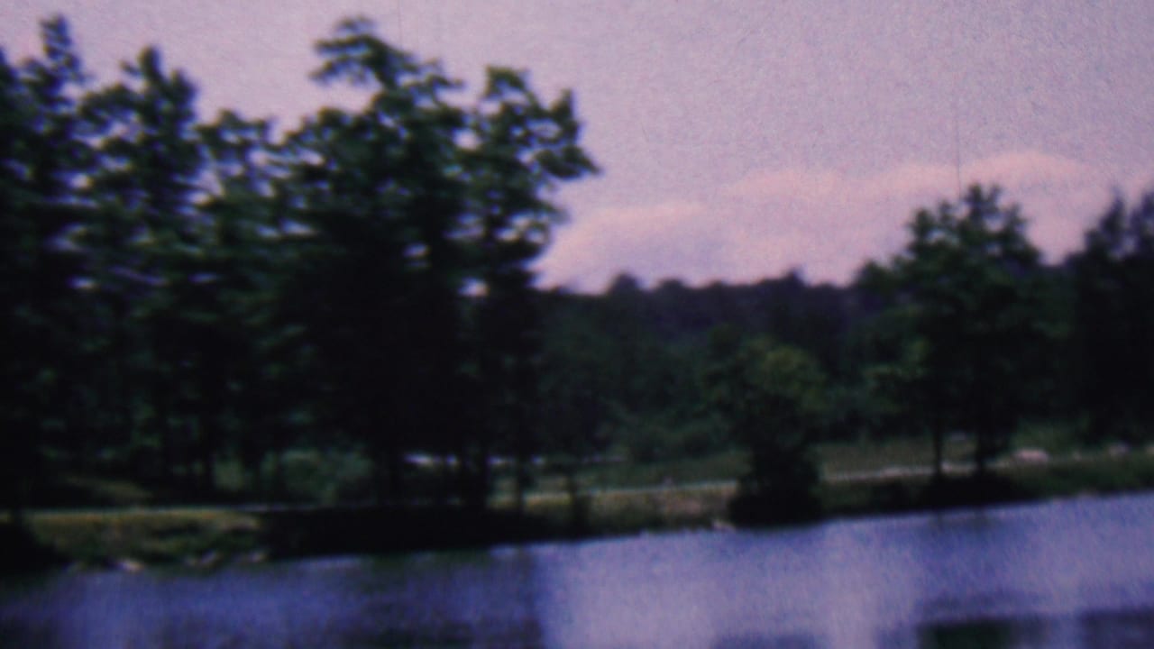 1961 8mm home-movie frame from the Covington, Kentucky metadata showing a dark wooded shoreline across calm water beneath a muted sky.