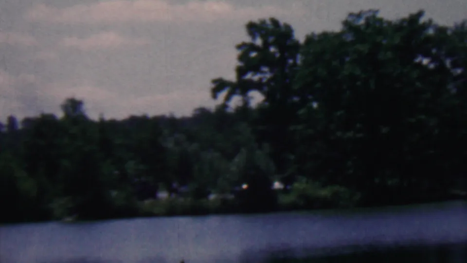 Final frame of the short 8mm pan shows dense lakeside foliage and water in the foreground, with no identifiable people or signage visible.