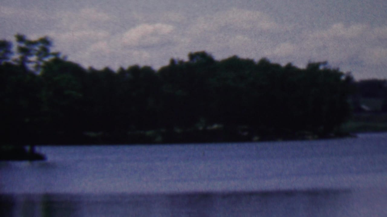 1961 8mm home-movie frame from the Covington, Kentucky metadata showing calm lake water, a distant wooded shore, and a cloudy sky.