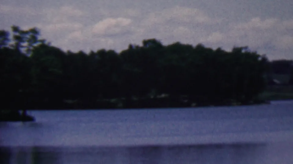 1961 8mm home-movie frame from the Covington, Kentucky metadata showing calm lake water, a distant wooded shore, and a cloudy sky.