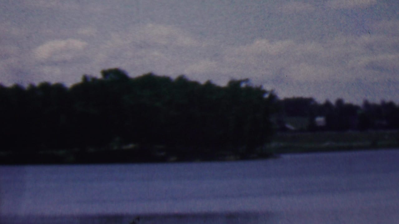 Lake surface with wooded shoreline and faint distant structures under clouds.