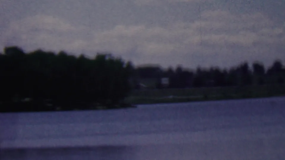 1961 8mm home-movie frame from the Covington, Kentucky metadata showing a wide lake view, trees at the left edge, and a distant grassy shoreline.