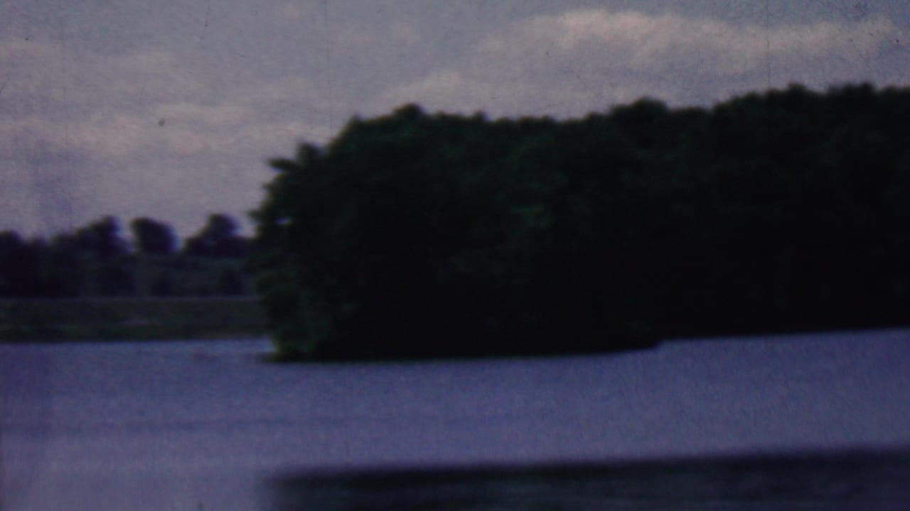 Wooded shoreline across a calm lake under a cloudy sky.
