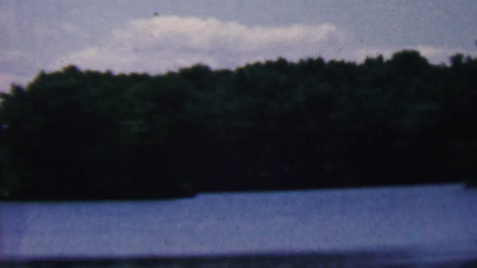 1961 Covington, Kentucky 8mm frame showing a darker band of trees along the far side of the lake and pale cloud cover above.
