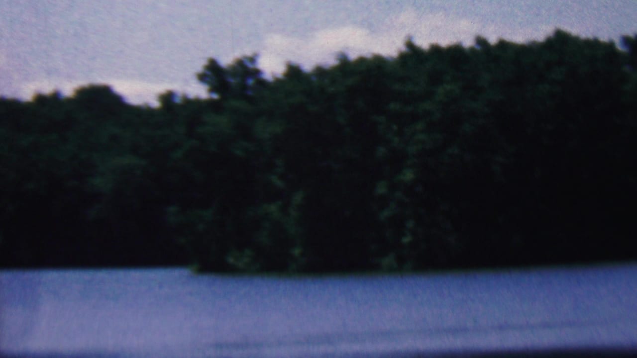 1961 8mm home-movie frame from the Covington, Kentucky metadata showing blue lake water, a dark green forest shoreline, and pale sky.