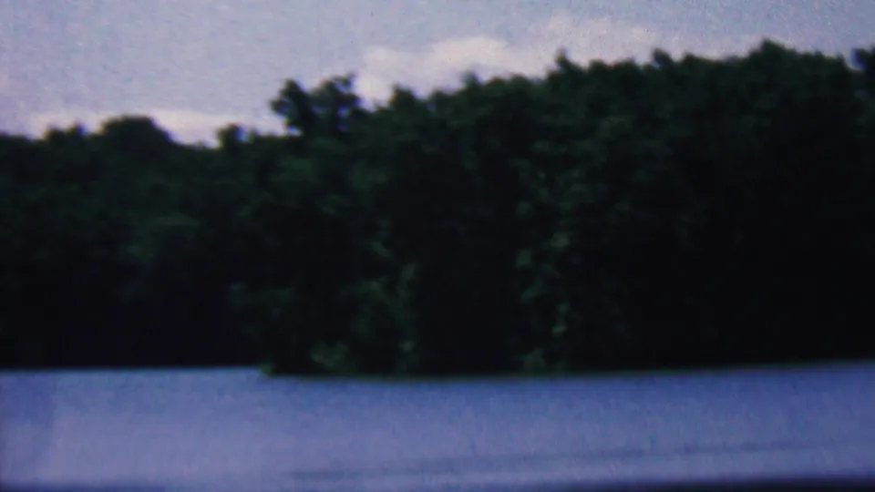 1961 8mm home-movie frame from the Covington, Kentucky metadata showing blue lake water, a dark green forest shoreline, and pale sky.