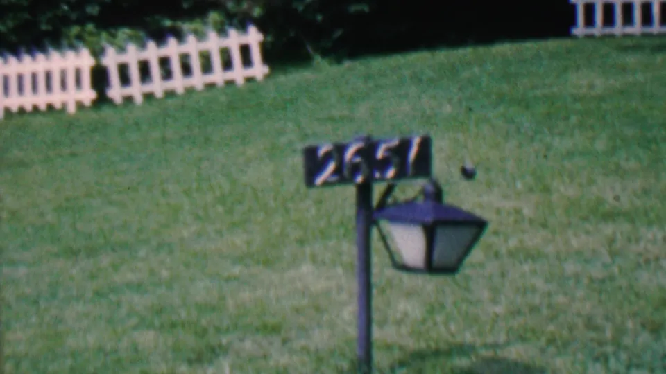 A residential lawn in Hatfield, Pennsylvania shows white fence sections and an address lamp post marked 2651 after the squirrel has moved out of the frame.
