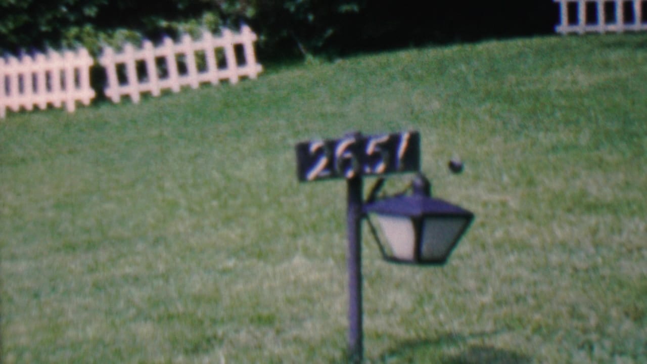 1956 Hatfield, Pennsylvania home-movie frame showing a black lamp post with the number 2651 in front of a green lawn and white picket fence sections.