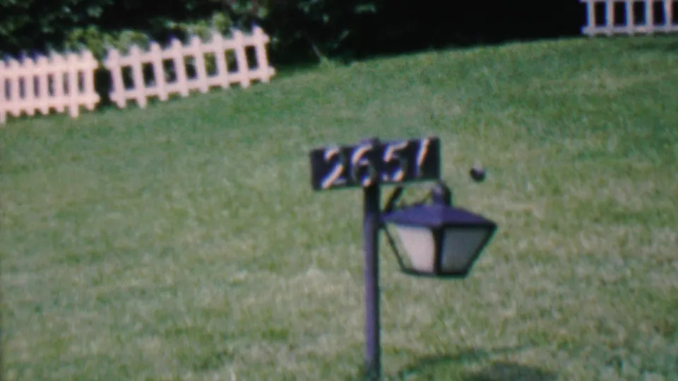 1956 Hatfield, Pennsylvania home-movie frame showing a black lamp post with the number 2651 in front of a green lawn and white picket fence sections.