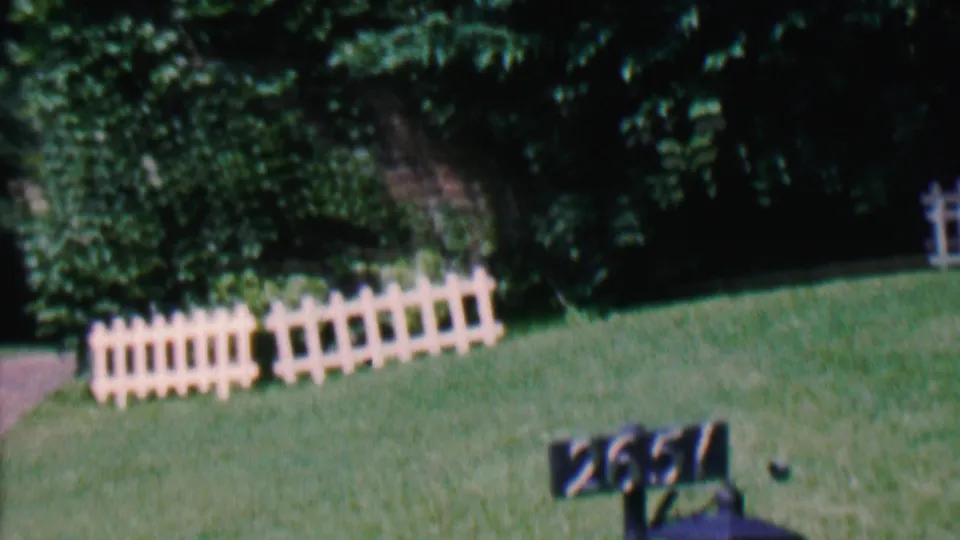 1956 Hatfield, Pennsylvania home-movie view widening to show the lamp post number 2651 below white fence sections and dense greenery.