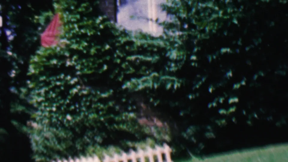 1956 Hatfield, Pennsylvania frame shifting away from the lamp post toward shrubs, lawn, white picket fencing, and a partial house exterior edge.