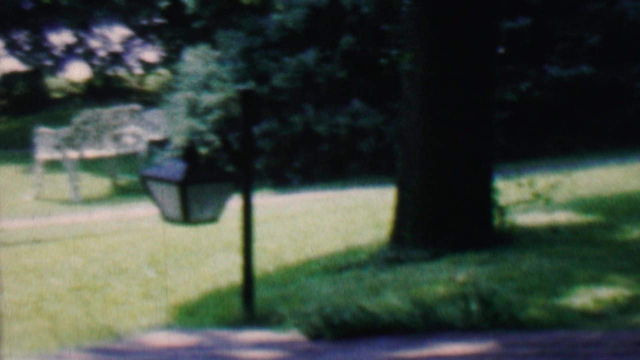 1956 Hatfield, Pennsylvania home-movie frame with a dark lamppost beside a path, a grassy yard, mature trees, and soft-focus landscaping in the background.