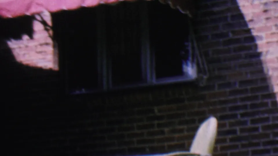 1956 Hatfield, Pennsylvania frame with a pink awning over a dark window on a red brick residential exterior, with part of patio furniture at the edge.
