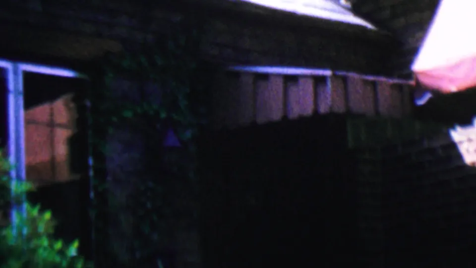 1956 Hatfield, Pennsylvania home-movie frame showing a shaded residential exterior with a window, awning edge, roofline, brickwork, and plants near the wall.