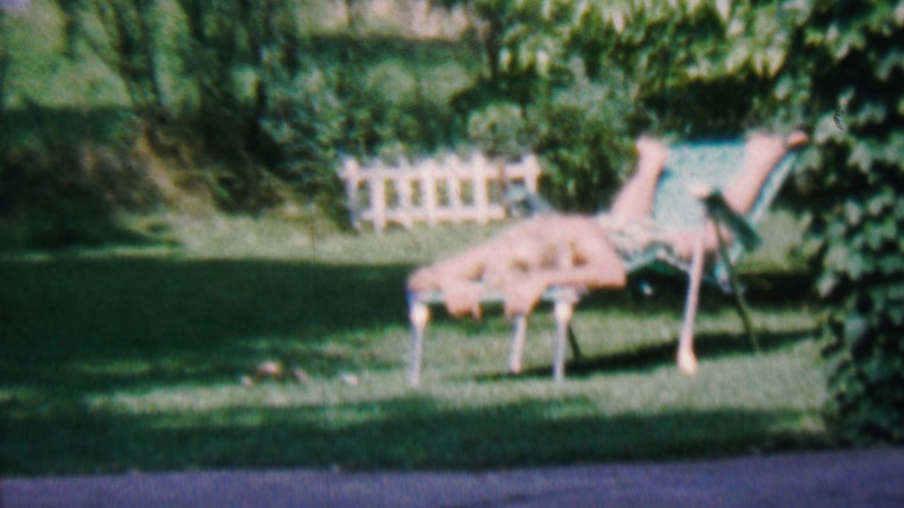 Woman reclining on a lawn chair in a green garden with white fencing behind her.