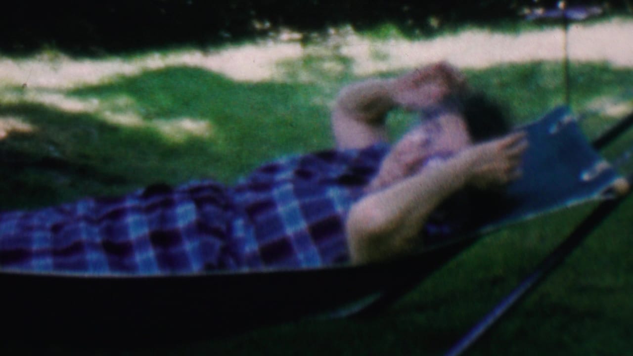 Woman lying in a blue hammock on a shaded grassy lawn.