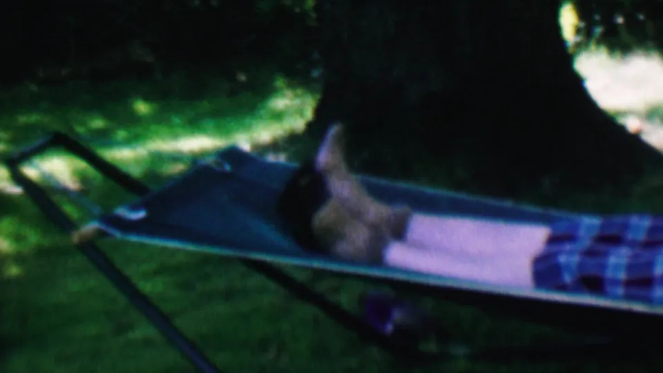 Final 1956 Hatfield, Pennsylvania frame showing the woman still reclined in the blue hammock, with dappled grass and heavy tree shade in the background.