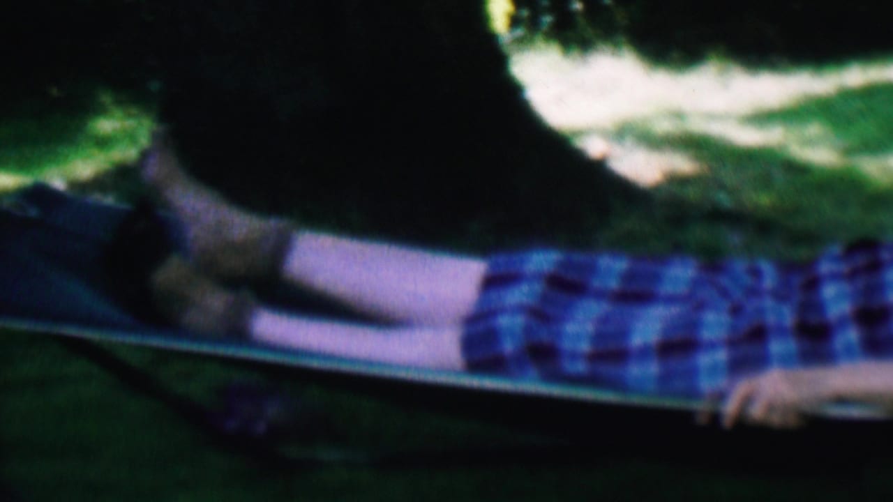 Older man reclines sideways in a hammock on a shaded lawn.