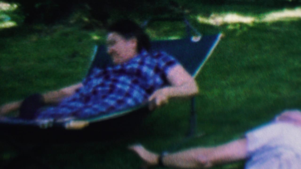 Man in a blue plaid shirt reclining in a lawn chair on grass.