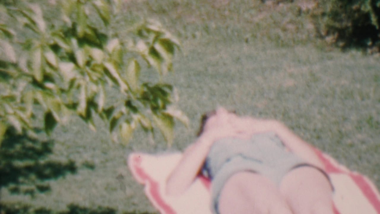 Woman reclines on a striped towel on the grass with one arm near her face.