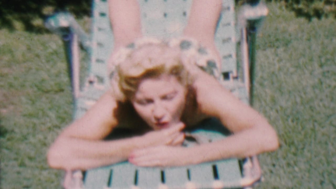 Adult woman on a lawn chair raises her face toward the camera while lying in the grass.