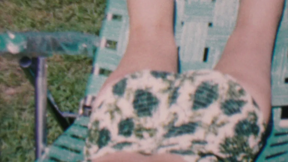 A closer handheld frame shows the woman's patterned swimsuit, legs, green lawn chair, and nearby grass in the sunny backyard setting documented as Hatfield, Pennsylvania in 1956.