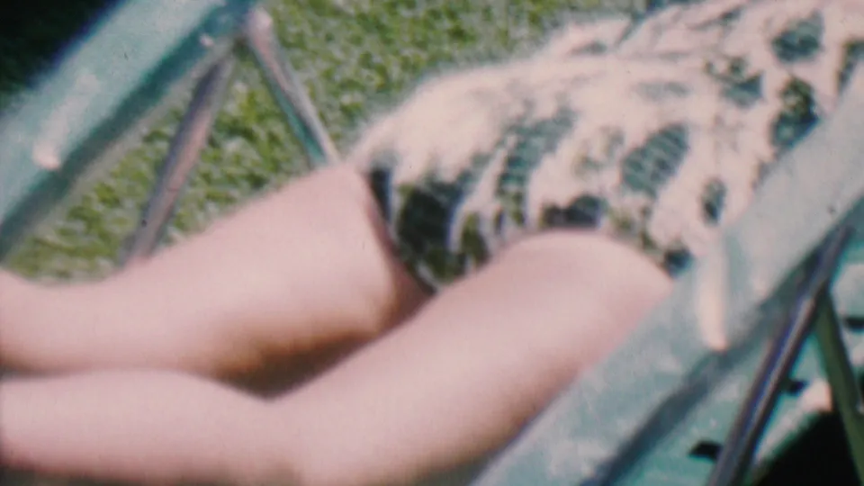 Hatfield, Pennsylvania home-movie frame from 1956 showing a person reclined on a green lawn chair, with the camera focused on the swimsuit and legs.