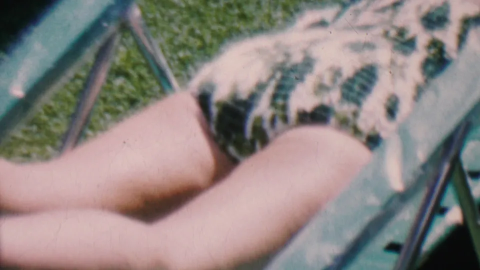 Soft-focus 1956 8mm frame showing a person in a patterned swimsuit reclining outdoors on a green lawn chair in Hatfield, Pennsylvania.