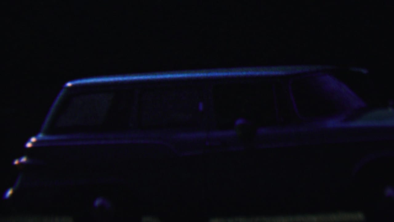 Dark nighttime view of a station wagon parked in shadow.
