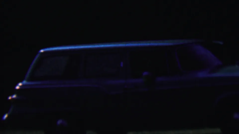 After-dark 1956 Hatfield, Pennsylvania home-movie frame showing a long station wagon in deep shadow with faint blue highlights.