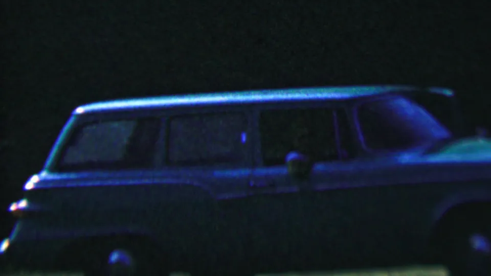 1956 Hatfield, Pennsylvania night frame showing the side of a station wagon with windows and chrome catching a blue glow in the darkness.