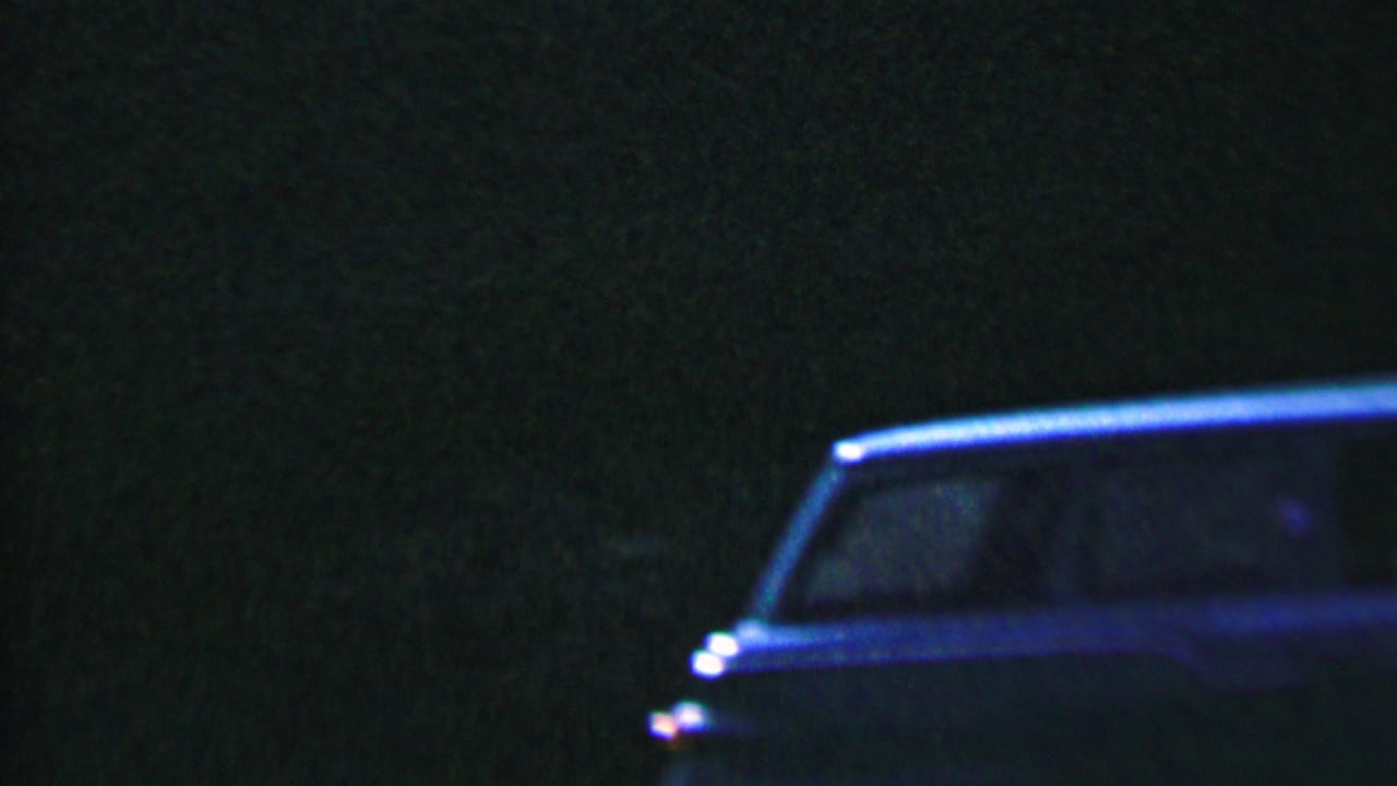 Dark, grainy frame with only faint shapes and blue-green shadow detail.