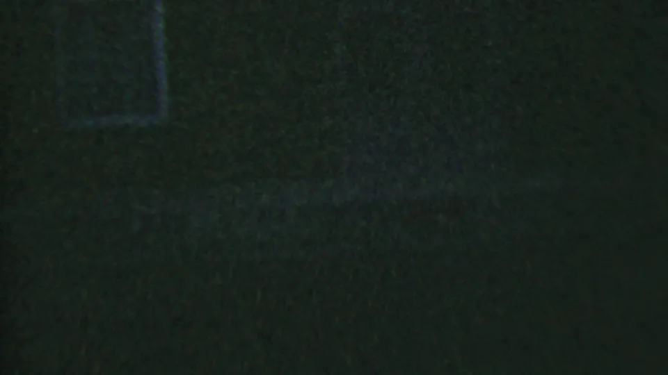 A partial view of the blue-tinted station wagon appears at the right edge of the frame, with its side windows and roofline emerging from the dark 8mm night scene.