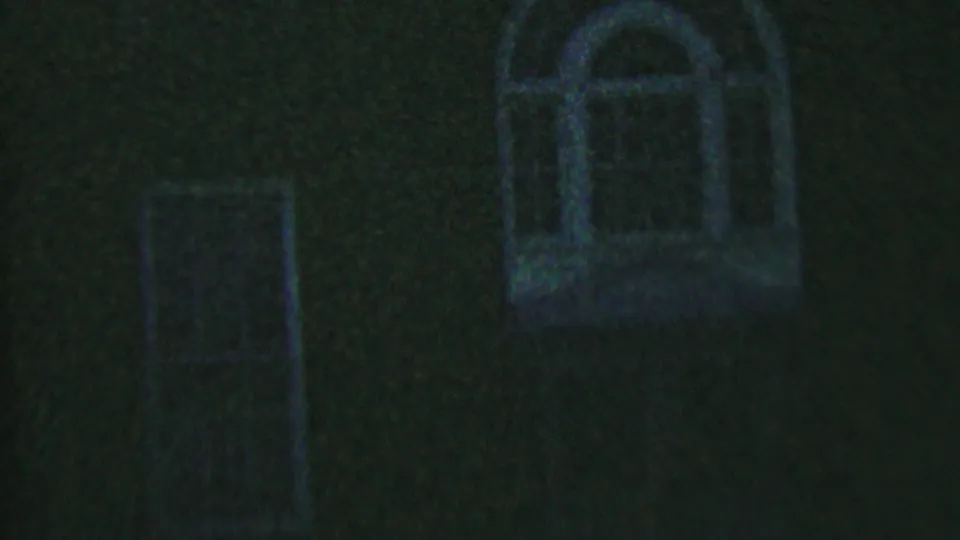 Low-light 8mm frame from Hatfield in 1956 showing a brick house wall with a central narrow window and a faint arched window near the upper right.
