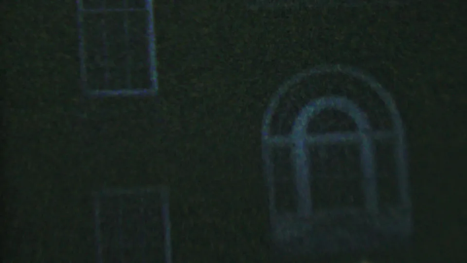 Dark 1956 home-movie frame in Hatfield, Pennsylvania with a prominent arched window, nearby rectangular window, and brick texture visible through heavy grain.